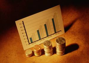 A chart showing upwards profits in front of increasing piles of coins.