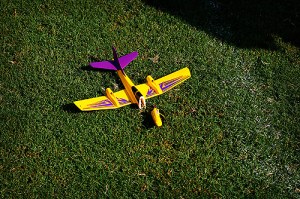 A yellow and purple toy plane that has crashed and broken on green grass.