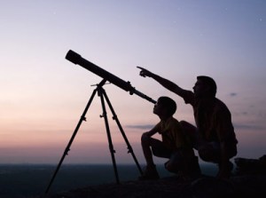 Two people use a telescope to look to the heavens. 